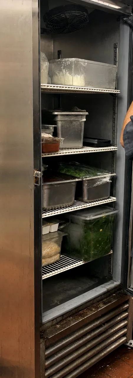 A narrow view into an open refrigerated cabinet, wire shelving loaded from top to bottom.